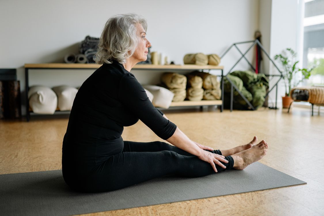 A senior woman practising a gentle seated stretch on a yoga mat at home